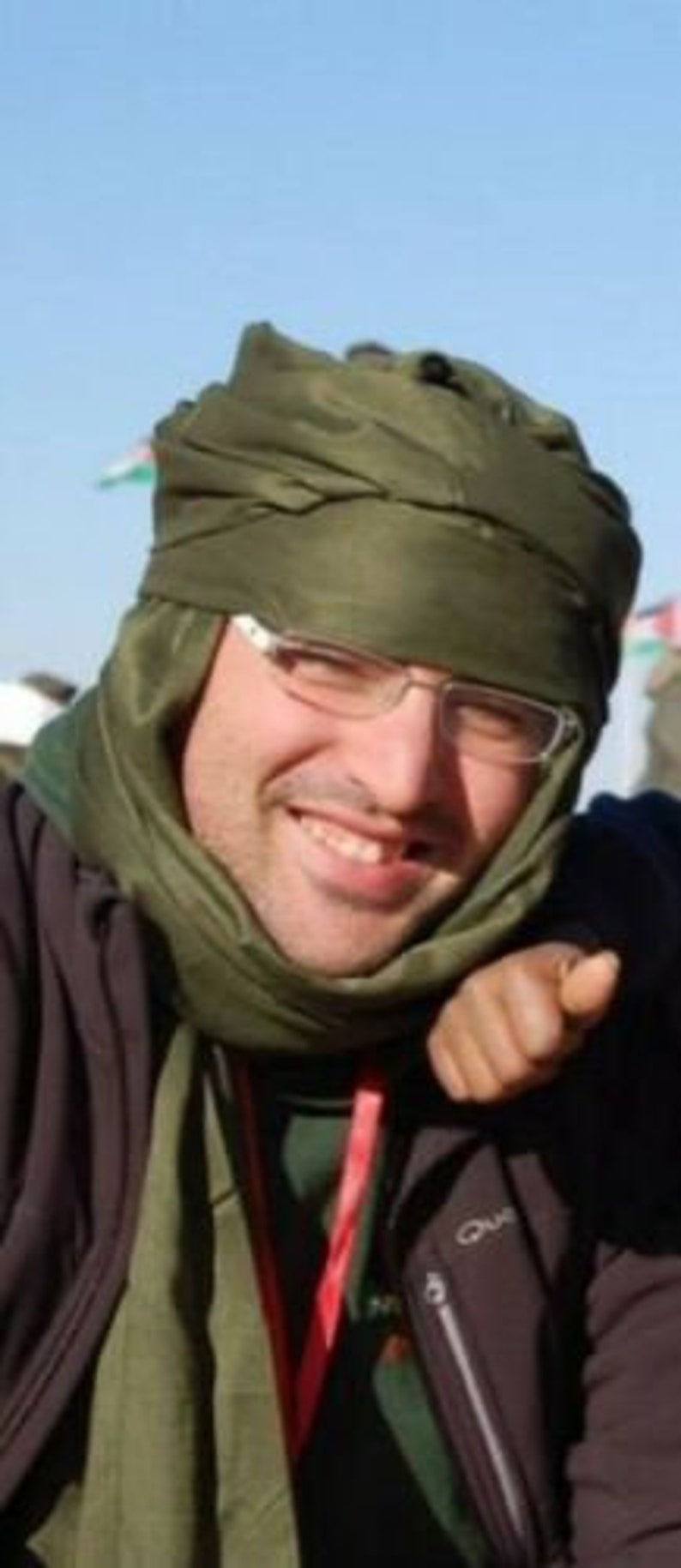 May include: A man wearing a green scarf and a black jacket with a red lanyard. He is smiling and looking at the camera.
