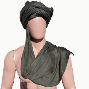May include: A dark green turban style head covering worn on a mannequin. The turban is made of a soft, drapey fabric.