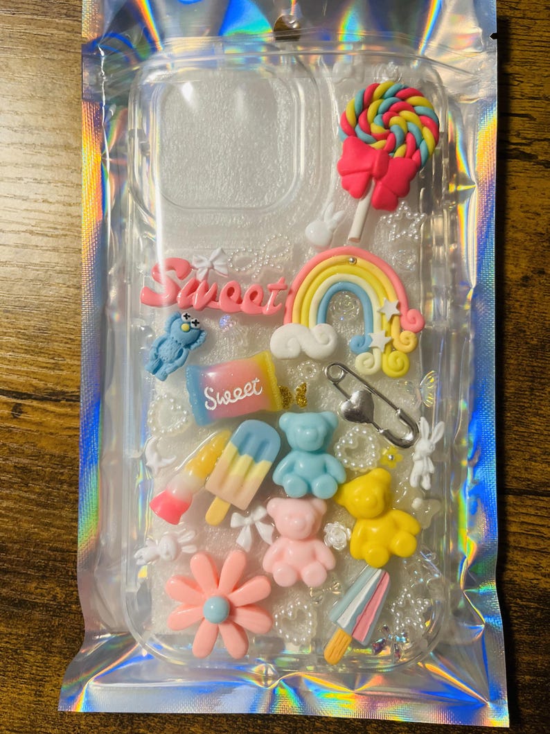 May include: A clear phone case with a rainbow, a lollipop, a gummy bear, a popsicle, a flower, and the word "Sweet" in pink letters.