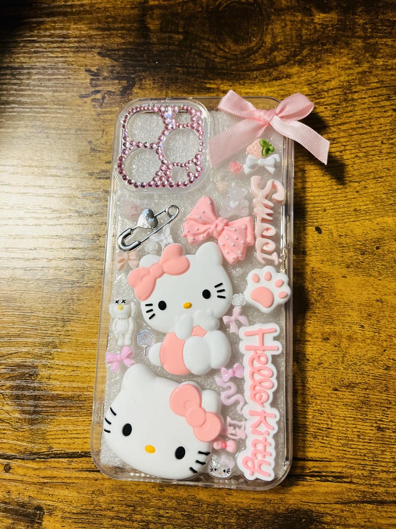 May include: A clear phone case with a pink glitter background. The case features a Hello Kitty design with two Hello Kitty figures, pink bows, and the text "Hello Kitty" and "Sweet".