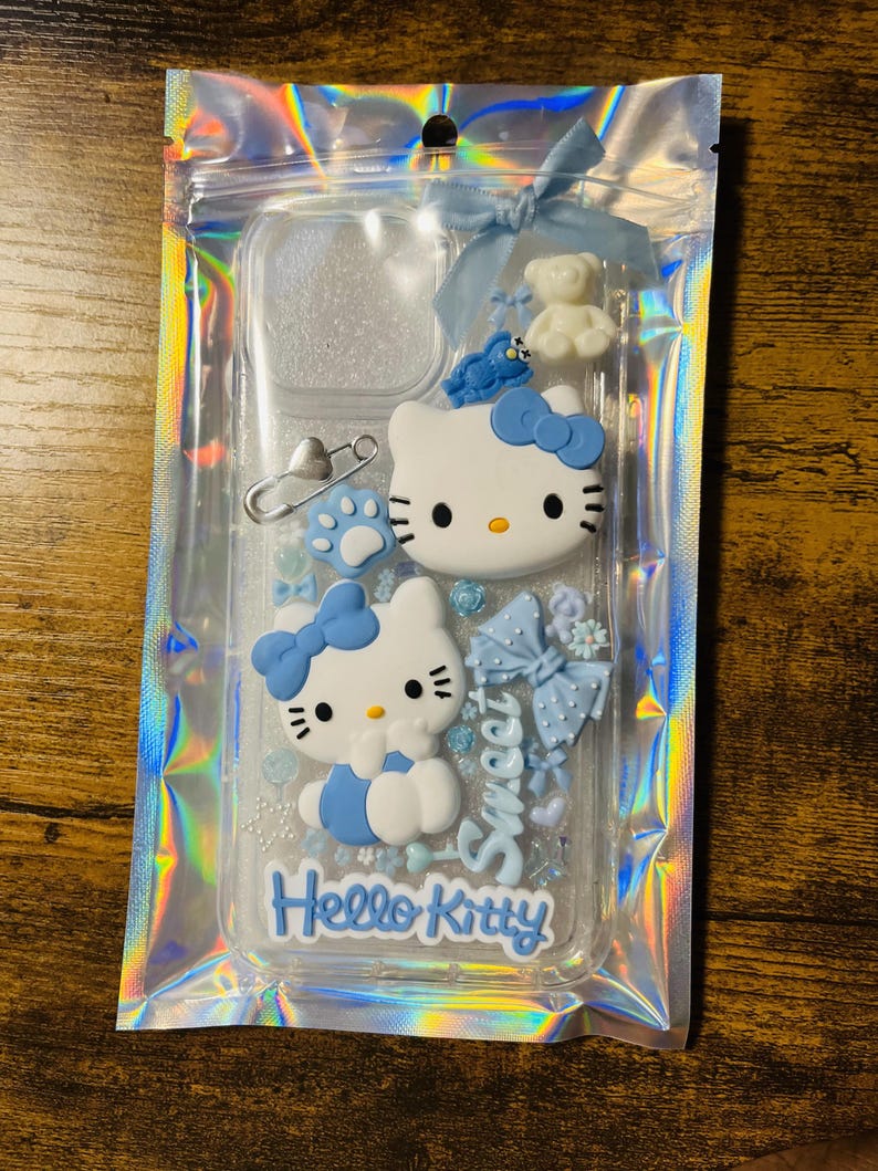 May include: A clear phone case with a blue Hello Kitty design. The case has glitter and various blue embellishments, including a bow, a teddy bear, and a paw print.