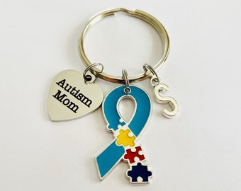 May include: A silver keychain with a blue ribbon with puzzle pieces, a heart charm that says "Autism Mom", and a letter "S" charm.