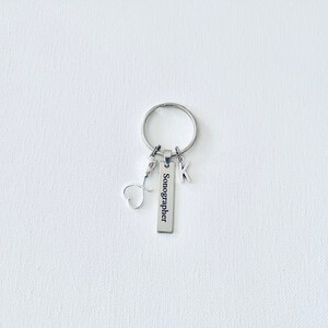 May include: Silver keychain with a heart charm, a letter K charm, and a rectangular tag that reads "Sonographer".