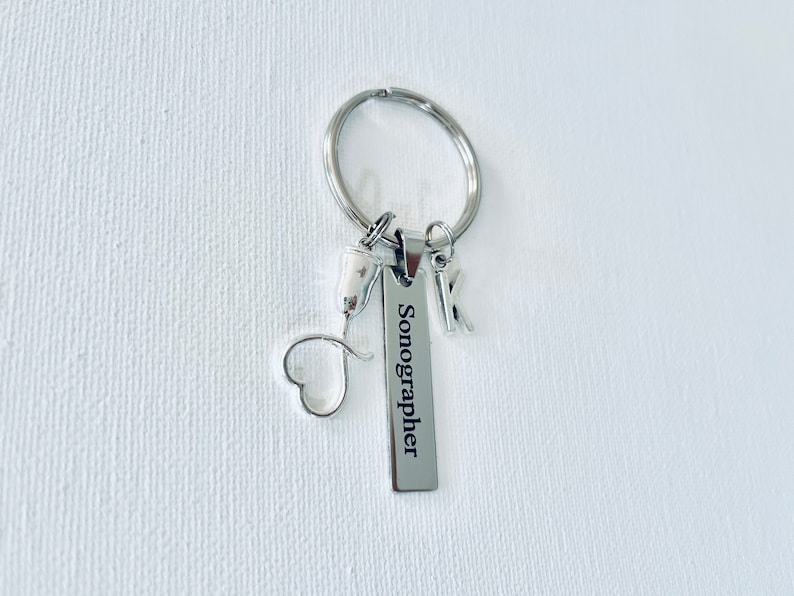 May include: Silver keychain with a heart charm, a small ultrasound probe charm, and a rectangular tag that reads "Sonographer".