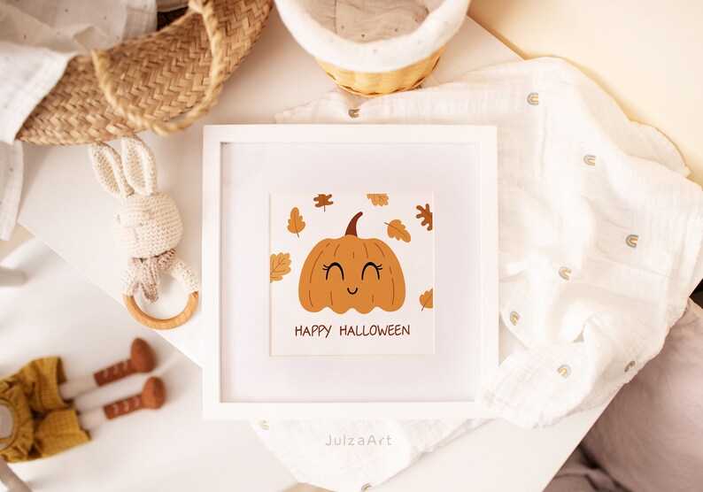 May include: A white framed print with a cute cartoon pumpkin with a smiling face and the text "Happy Halloween". The pumpkin is surrounded by orange and brown leaves.