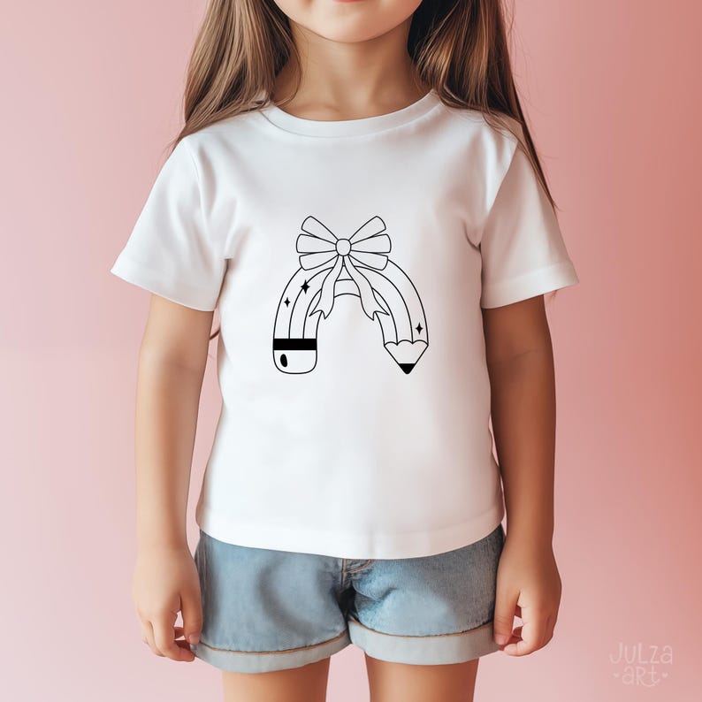 Op de afbeelding: Wit T-shirt met een zwart-wit potloodontwerp en een strik. Het potloodontwerp heeft een strik aan de bovenkant en sterren. Het shirt wordt door een kind gedragen.