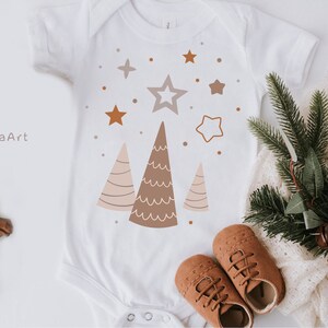 Puede incluir: Un body blanco para beb&eacute; con un dise&ntilde;o de &aacute;rbol de Navidad marr&oacute;n, rosa y blanco. El body tiene una estrella y peque&ntilde;os puntos en el fondo. El texto "JulzaArt" est&aacute; en la esquina superior izquierda.