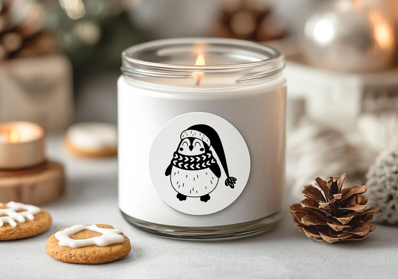 K&ouml;nnte beinhalten: Wei&szlig;e Kerze mit einer schwarz-wei&szlig;en Pinguin-Illustration auf dem Etikett. Der Pinguin tr&auml;gt einen Hut und einen Schal. Die Kerze befindet sich in einem Glasgef&auml;&szlig; mit einem wei&szlig;en Deckel.
