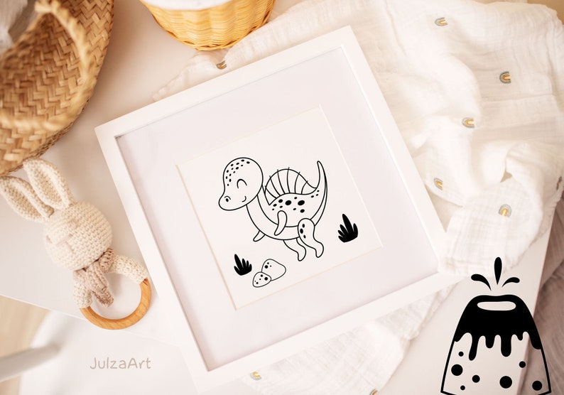 May include: Black and white line art print of a cartoon dinosaur with a spiky back, surrounded by small rocks and plants. The print is framed in a white frame and is sitting on a white surface.
