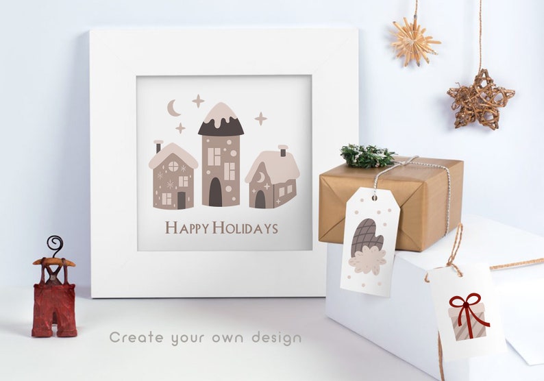 Puede incluir: Un marco blanco con una impresi&oacute;n de tres casas marrones con nieve en los techos y el texto "Happy Holidays". El marco est&aacute; sobre una superficie blanca con dos etiquetas de regalo, una con una manopla marr&oacute;n y la otra con una caja de regalo roja y blanca a rayas.