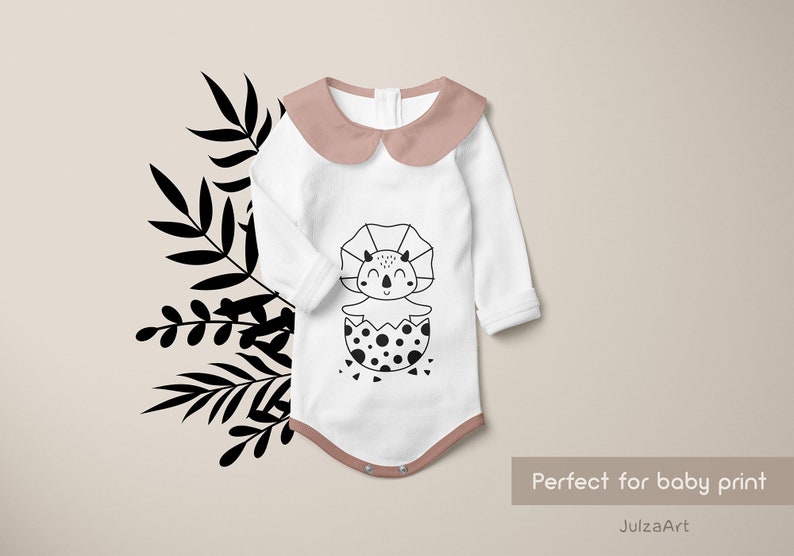 May include: White baby onesie with a pink collar and a black and white illustration of a dinosaur hatching from an egg. The text "Perfect for baby print" and "JulzaArt" are visible below the onesie.