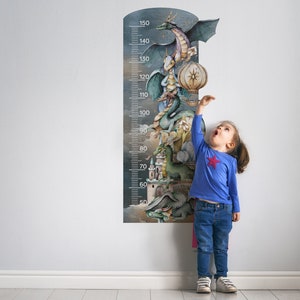 Può includere: Un bambino sta accanto a un grafico di altezza colorato con un design fantasioso di draghi e un castello. Il grafico è contrassegnato da numeri da 50 a 150.