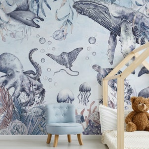 May include: A watercolor mural depicting a blue whale, octopus, stingray, jellyfish, and other sea creatures on a light blue background. The mural is in a child's bedroom with a wooden bed frame and a blue armchair.