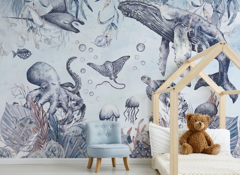 May include: A watercolor mural depicting a blue whale, octopus, stingray, jellyfish, and other sea creatures on a light blue background. The mural is in a child's bedroom with a wooden bed frame and a blue armchair.