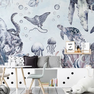 May include: A watercolor mural depicting an underwater scene with an octopus, a stingray, a turtle, jellyfish, and coral. The mural is painted on a light blue background with white bubbles. The mural is displayed in a child's room with a white table and chairs, a white bookshelf, and a white stuffed animal.