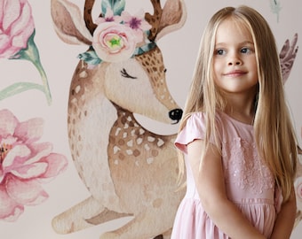 May include: A young girl with long blonde hair is standing in front of a pink and brown watercolor illustration of a deer wearing a floral crown. The deer has closed eyes and is looking down. The girl is wearing a pink dress with sequins.