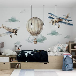 May include: A child's bedroom decorated with an aviation theme. The wall has watercolour illustrations of aeroplanes, clouds, and a hot air balloon. The room includes a bed, storage, soft toys, and a blue rucksack.