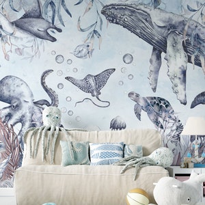 May include: A watercolor mural featuring a blue whale, octopus, stingray, and sea turtle. The mural is painted on a light blue background with white bubbles. The mural is displayed in a room with a white couch and pillows.