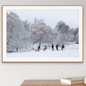 May include: A snowy winter scene with a group of people sledding down a hill in a park. The trees are covered in snow and the sky is overcast.