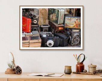 Può includere: Una collezione di macchine fotografiche vintage e contenitori di pellicola di varie dimensioni e colori, tra cui nero, marrone, rosso e argento. Le macchine fotografiche sono disposte in una pila, con alcune impilate una sopra l'altra. Ci sono anche diverse scatole e lattine, alcune con immagini di persone e paesaggi. Gli oggetti sono disposti su una superficie di legno.