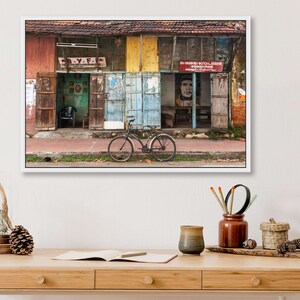 May include: A weathered, multi-colored building with a bicycle parked in front. The building has several doors and windows, and the walls are covered in faded paint and posters. The bicycle is black with a brown seat and handlebars.