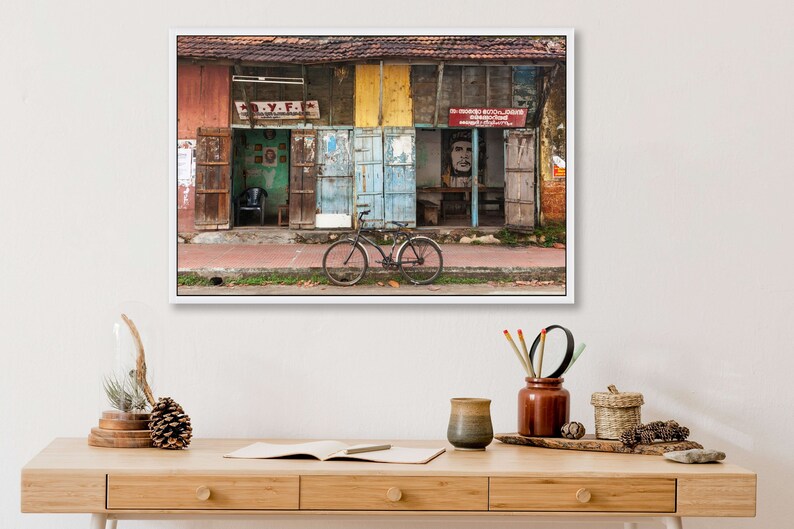 May include: A weathered, multi-colored building with a bicycle parked in front. The building has several doors and windows, and the walls are covered in faded paint and posters. The bicycle is black with a brown seat and handlebars.