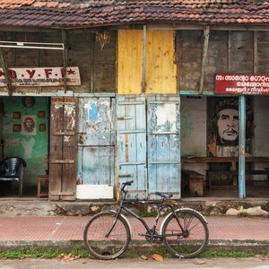 May include: A weathered wooden building with two open doorways. The building has a red, yellow, and blue paint scheme. A bicycle is parked in front of the building. The sign above the doorway on the left reads "D.Y.F.". The sign above the doorway on the right is in a foreign language.