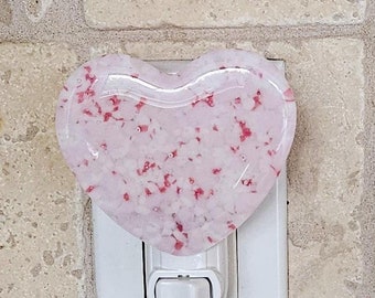 Könnte beinhalten: Ein herzförmiges Nachtlicht mit einem rosa-weißen, gesprenkelten Design. Das Nachtlicht ist an eine normale Steckdose angeschlossen.