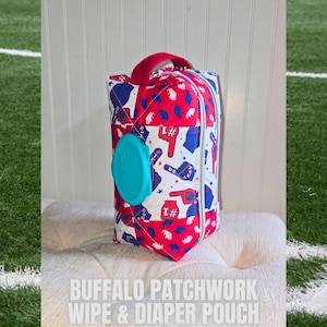 May include: A quilted wipe and diaper pouch with a red handle and a blue, red, and white patchwork design. The pouch has a turquoise lid and a silver zipper. The text "BUFFALO PATCHWORK WIPE & DIAPER POUCH" is displayed on the bottom.