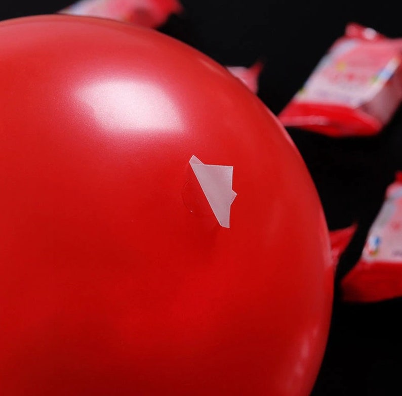 May include: A bright red balloon with a small white piece of tape covering a hole.