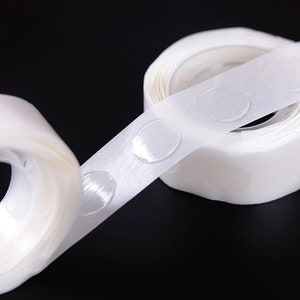 May include: A roll of white adhesive tape with clear, round, sticky dots. The tape is designed for attaching balloons, decorations, or other lightweight items to walls or ceilings.