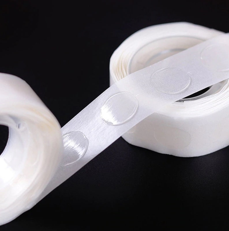 May include: A roll of white adhesive tape with clear, round, sticky dots. The tape is designed for attaching balloons, decorations, or other lightweight items to walls or ceilings.