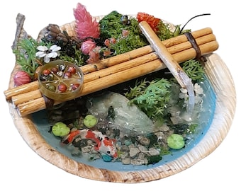 Puede incluir: Un jardín zen en miniatura con un pequeño estanque, un puente de madera y una cascada. El estanque está lleno de resina azul y tiene pequeños nenúfares verdes y peces koi naranja y blancos. El jardín está rodeado de musgo verde, flores rosas y una piña.