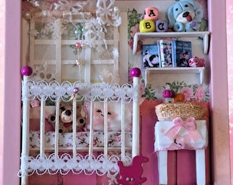 May include: A pink framed miniature nursery scene with a white crib, a rocking horse, a small table with a basket, and a shelf with books and a blue toy dog. The crib has a white lace trim and a pink and white floral patterned bedding. The rocking horse is pink and white. The table is white with a pink and white floral patterned tablecloth. The shelf is white with a pink and white floral patterned background. The books are colorful and have titles like "The Little Engine That Could" and "The Very Hungry Caterpillar". The toy dog is blue and white and has a red nose.