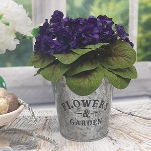 Konstgjorda afrikanska violer, hellila. Rund lantlig metallvas med handtag. Krukväxt, rustik.