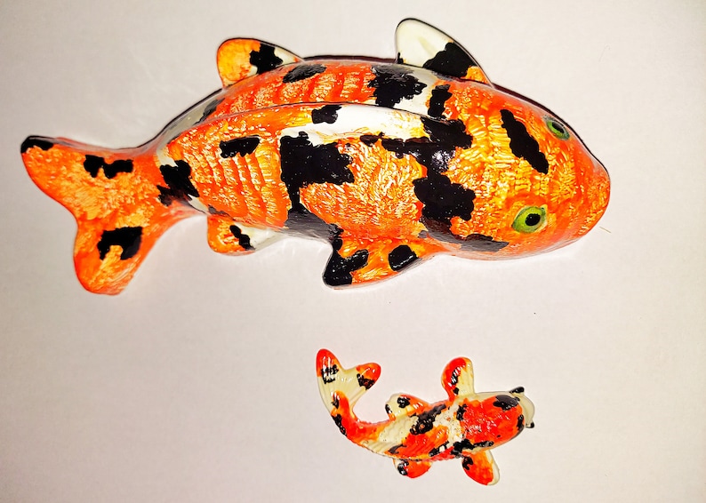 Puede incluir: Dos peces koi de cer&aacute;mica pintados a mano, uno grande y otro peque&ntilde;o. El pez m&aacute;s grande es naranja y negro con detalles blancos. El pez m&aacute;s peque&ntilde;o es naranja, negro y blanco.