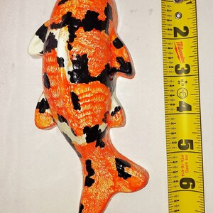 Puede incluir: Una figurita de pez koi pintada a mano en naranja, negro y blanco. La figurita mide aproximadamente 15 cm de largo y est&aacute; hecha de un material similar a la cer&aacute;mica.