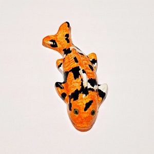 Op de afbeelding: Een klein, oranje en zwart keramiek koi-visje met witte accenten en groene ogen.