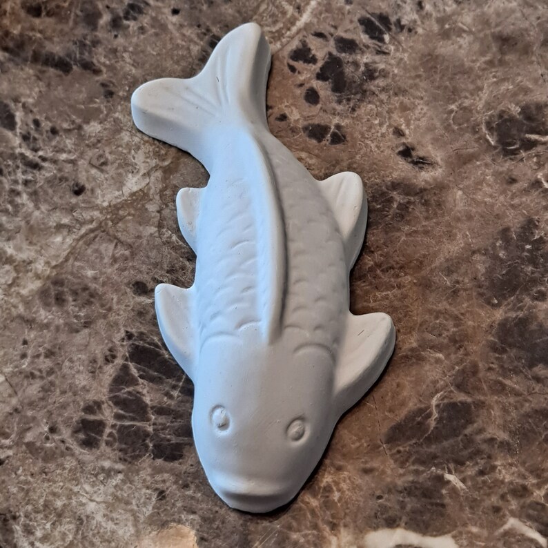 Puede incluir: Figurita de pez de cer&aacute;mica blanca con un dise&ntilde;o detallado. El pez tiene la boca ligeramente hacia arriba y ojos grandes.