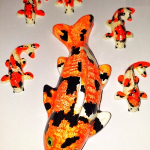 Puede incluir: Cinco figuritas de peces koi de cer&aacute;mica en varios tama&ntilde;os. El pez m&aacute;s grande es naranja y negro con detalles blancos. Los peces m&aacute;s peque&ntilde;os son naranja, negro y blanco.