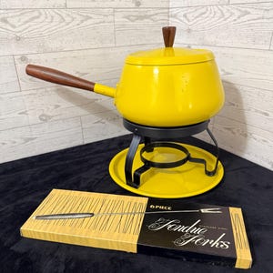 May include: A bright yellow fondue pot with a dark brown wooden handle and lid knob, resting on a black metal stand and base. In front, a rectangular box features the text "6 PIECE" and "Fondue Forks" with a graphic illustration of a fork.