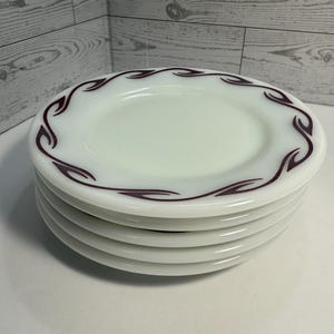 May include: A stack of six white plates with a decorative maroon leaf-like pattern around the rim. The plates are stacked neatly on top of each other, showcasing a clean and classic design.