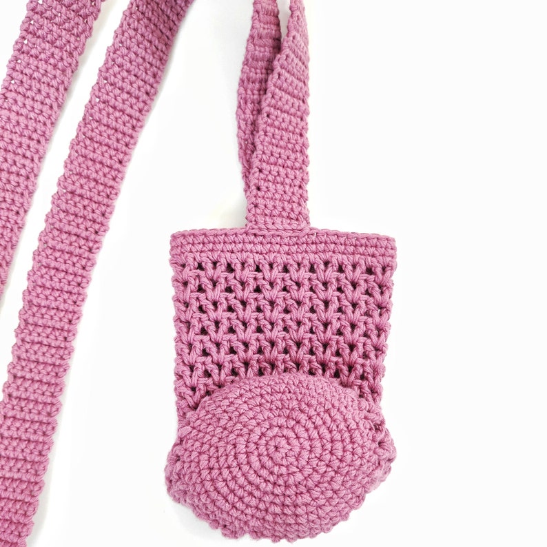 A pink crocheted bag with a round bottom and two long straps. The bag is made with a delicate stitch pattern.