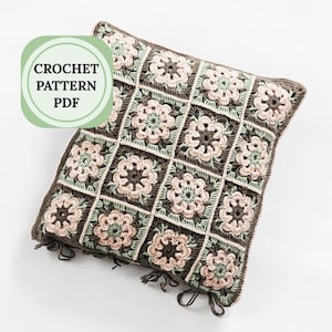 Könnte beinhalten: Quadratisches Häkelkissen mit einem Blumenmuster in Braun-, Rosa- und Grüntönen. Das Kissen hat einen dunkelbraunen Rand und Quasten. Der Text "CROCHET PATTERN PDF" befindet sich in einem grünen Kreis oben links.