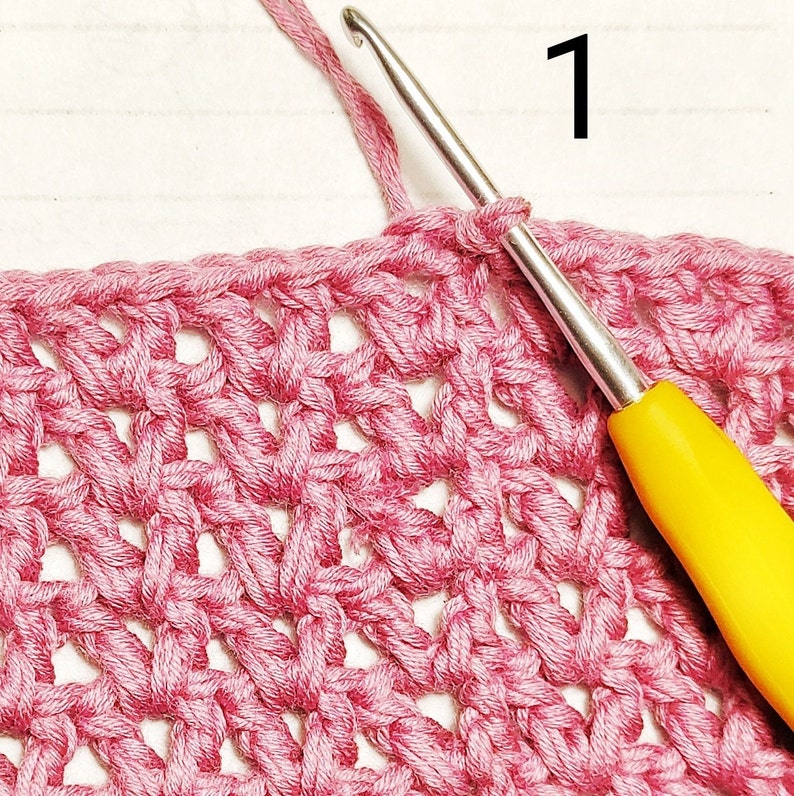 A close-up of a crochet project in progress. The crocheter is using a pink yarn and a yellow crochet hook. The number "1" is written on the white background.