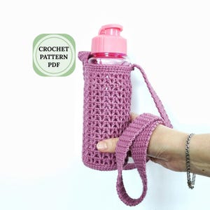 A pink crocheted water bottle holder with a strap. The holder is made with a simple stitch pattern and has a light pink color. The text "CROCHET PATTERN PDF" is on a green square.