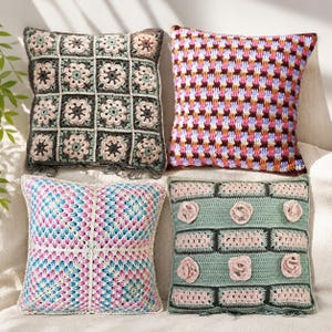 Puede incluir: Cuatro cojines cuadrados de ganchillo. Uno presenta cuadrados de la abuela florales en gris oscuro y rosa con flecos. Otro tiene un patrón de cuadros multicolor. Un tercero muestra un diseño radial azul y rosa. El cuarto es verde salvia con rosetas rosas.