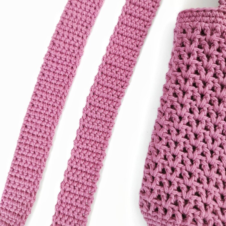 Two pink crocheted straps and a pink crocheted bag. The straps are made with a single crochet stitch and the bag is made with a more intricate stitch.