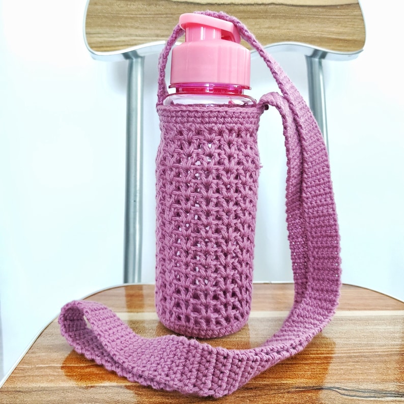 A pink water bottle with a crocheted pink sleeve and a long pink crocheted strap.
