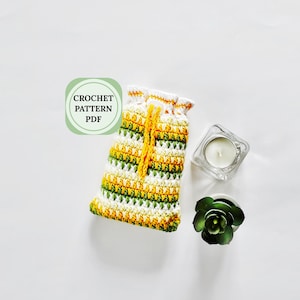May include: A crocheted drawstring bag in yellow, green, and white, with a yellow drawstring. The bag is next to a small candle in a glass holder and a small succulent plant. Text on the left says "CROCHET PATTERN PDF".